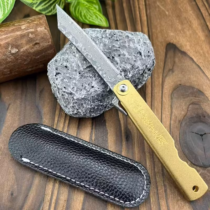 Higonokami Damascus folding knife with copper alloy handle and leather slip on wood