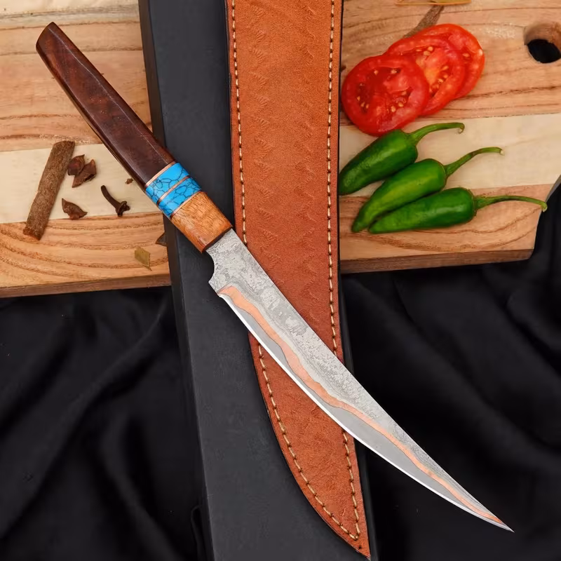 Copper Damascus fillet knife with layered copper Damascus blade and leather sheath on a cutting board
